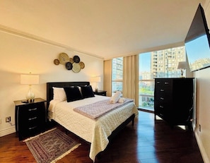 Ein Schlafzimmer mit einem Bett, Nachttischen, einer Kommode und einem großen Fenster mit Blick auf die Stadt.