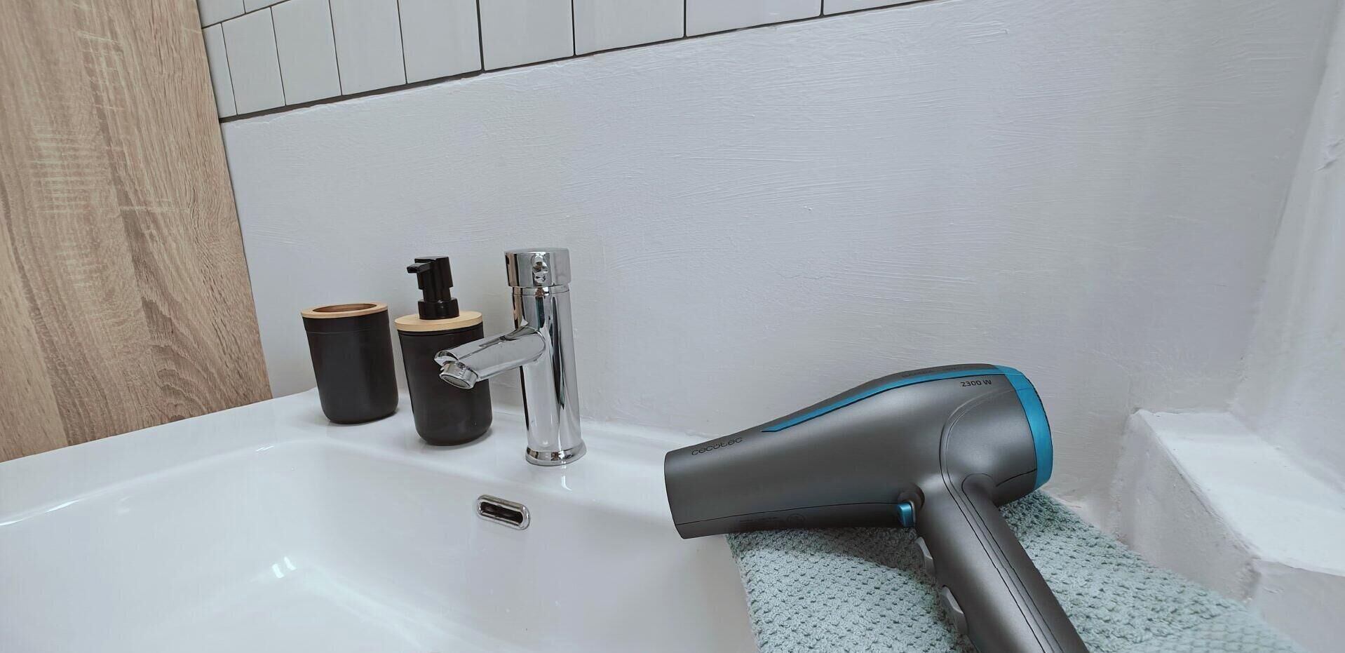 Une salle de bain avec une baignoire blanche, un sèche-cheveux et deux récipients noirs.
