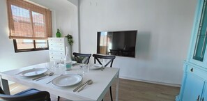 A dining area with a white table set for four, a TV mounted on the wall, and a blue cabinet.