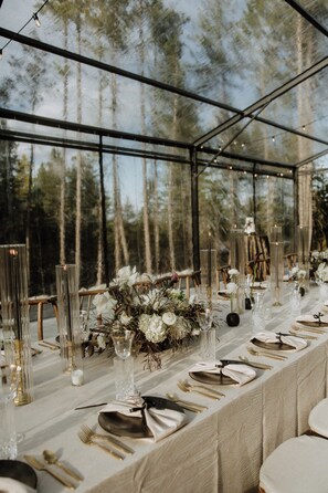 Een lange tafel gedekt voor een formeel evenement, met hoge glazen kandelaars, witte bloemen en gouden bestek.