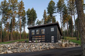 A modern two-story cabin with a garage, surrounded by a forest.
