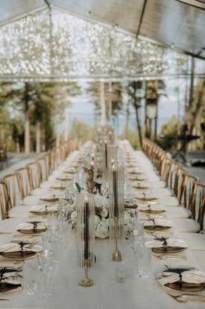 Een lange tafel gedekt voor een formeel evenement, met witte tafelkleden, gouden bestek en heldere glazen.