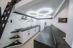 A modern kitchen with a long countertop, white cabinets, and a hexagonal ceiling light fixture.