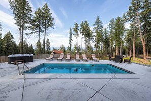 A rectangular swimming pool with a tiled deck, surrounded by lounge chairs and a hot tub.
