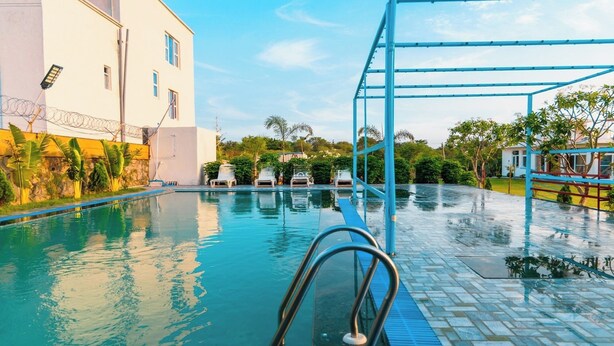 Una piscina con estructura metálica azul, sillas de descanso y un edificio con ventanas de rejas.