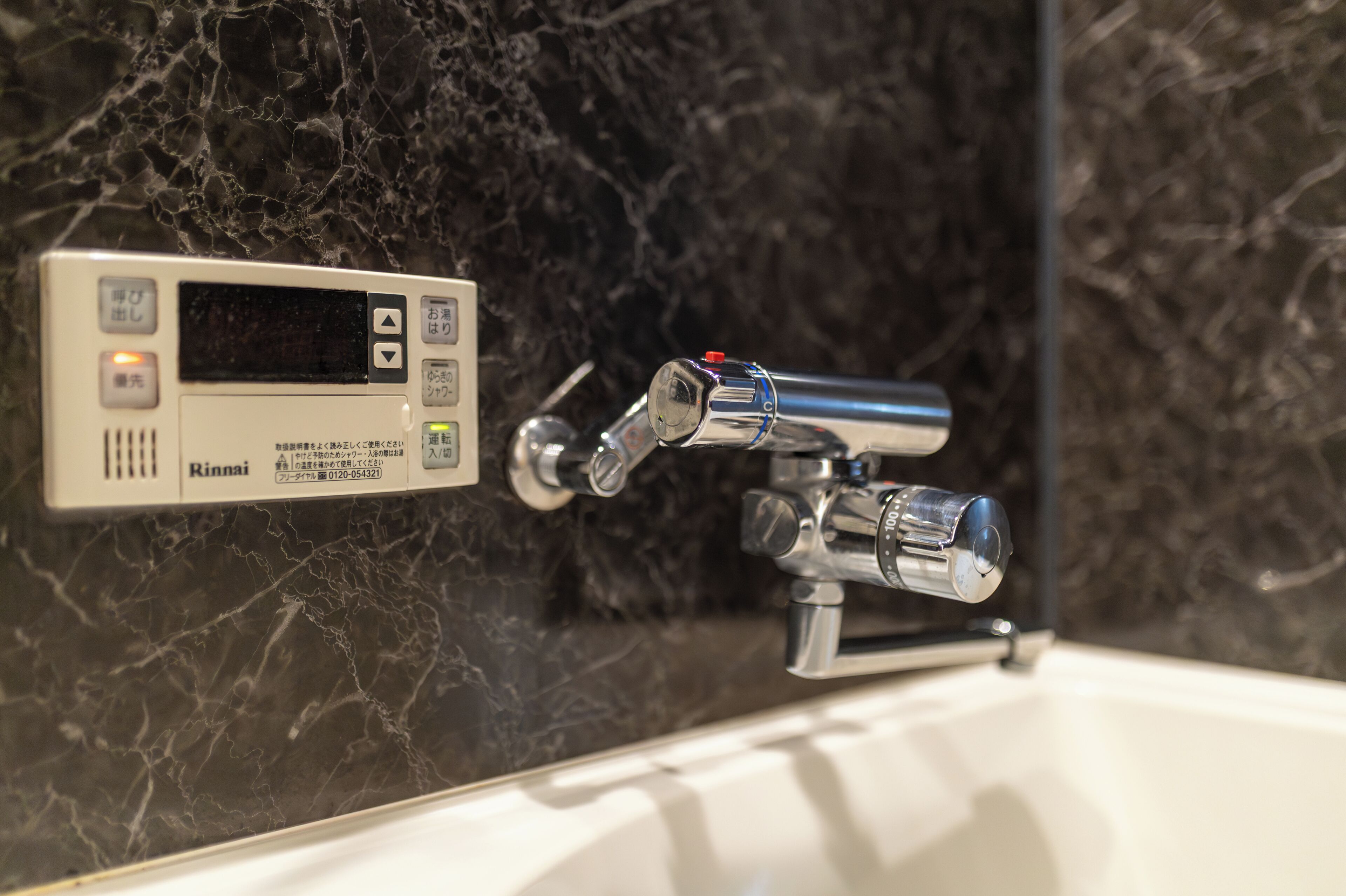 A bathroom with a digital control panel, a chrome faucet, and a marble wall.