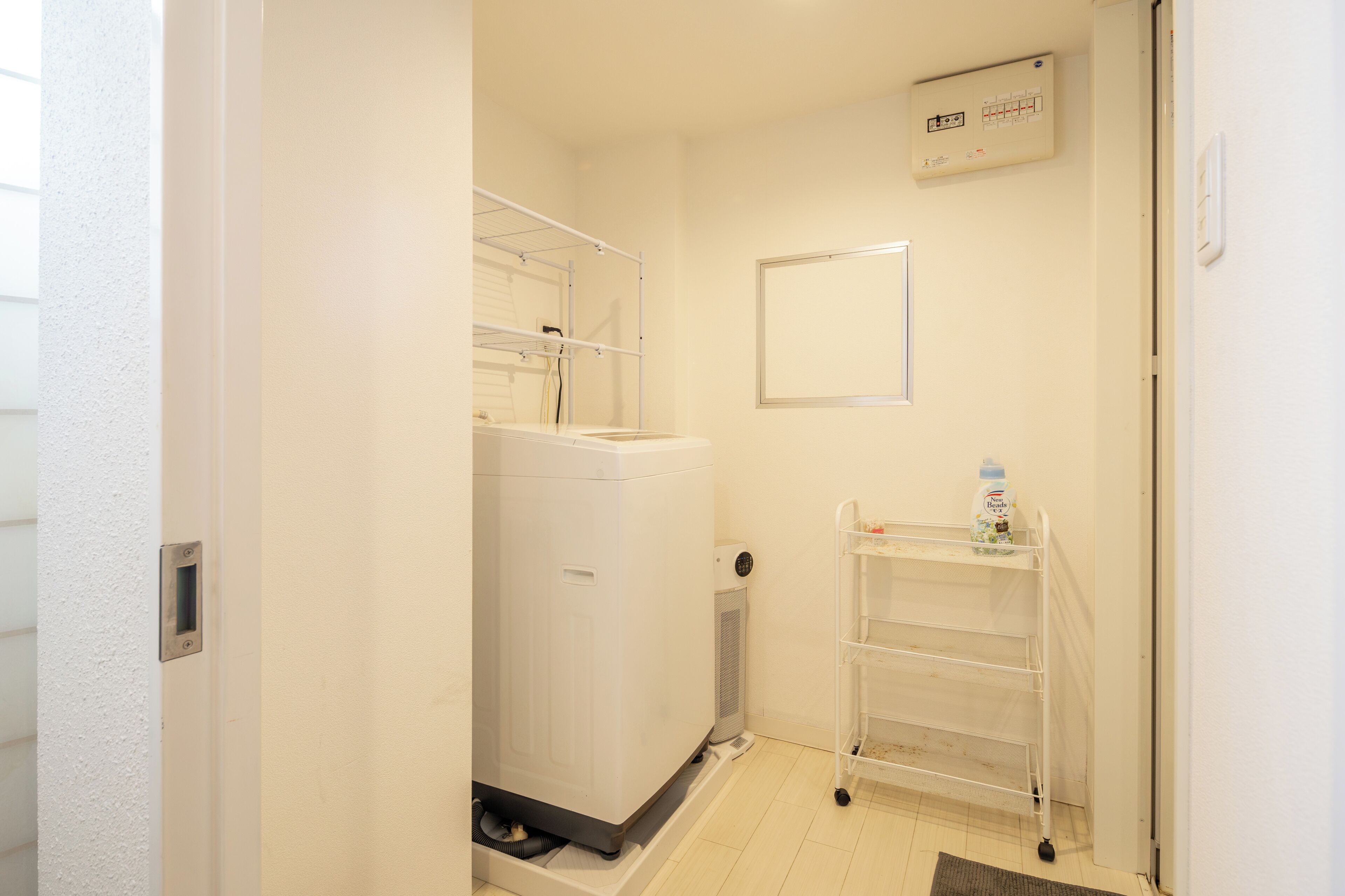 A compact bathroom with a washing machine, a drying rack, and a shelf with a bottle.