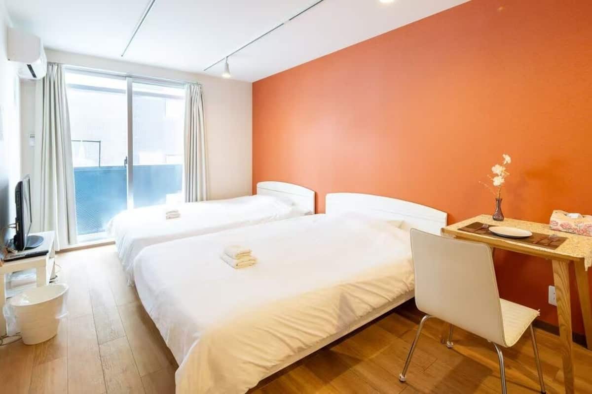 Quarto de hotel com duas camas, uma escrivaninha com cadeira, televisão e janela com cortinas.