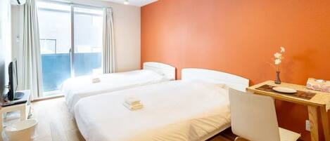 A hotel room with two beds, a desk with a chair, a television, and a window with curtains.