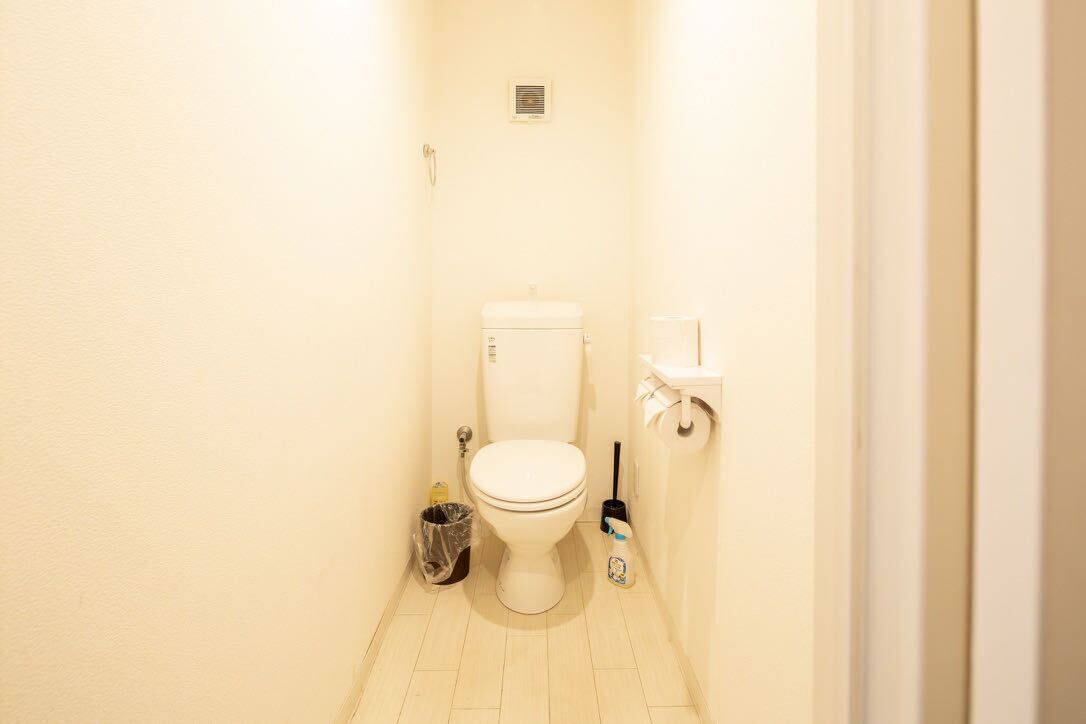 A small, white bathroom with a toilet, a trash can, and a cleaning brush.