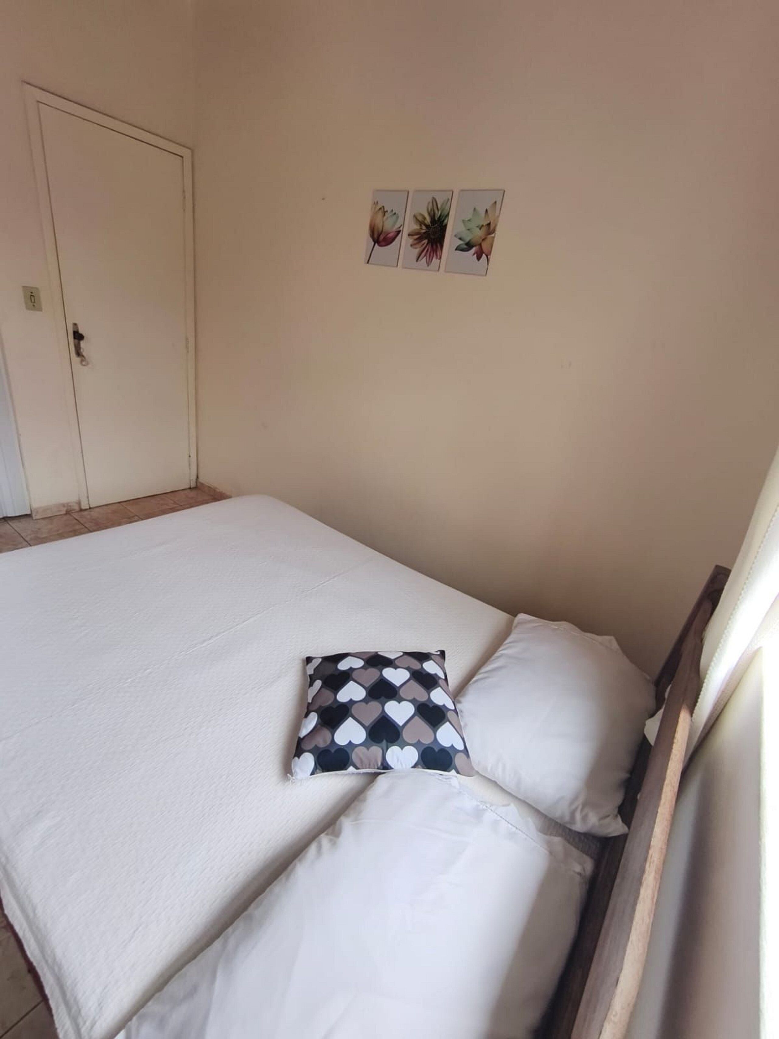 A single bed with white bedding and a heart-patterned pillow, a door, and three wall-mounted pictures.