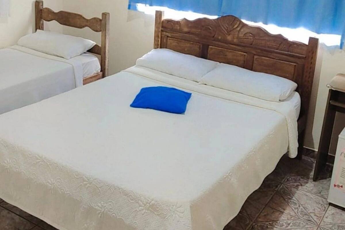 A bedroom with two single beds, a wooden headboard, a blue curtain, and patterned floor tiles.