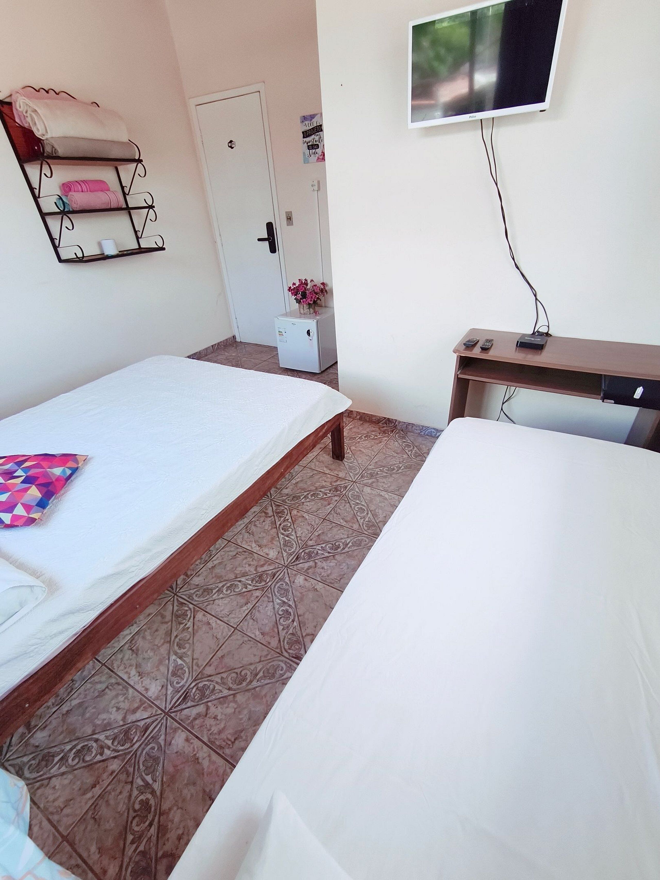 A room with two beds, a small desk, a TV, and a refrigerator.