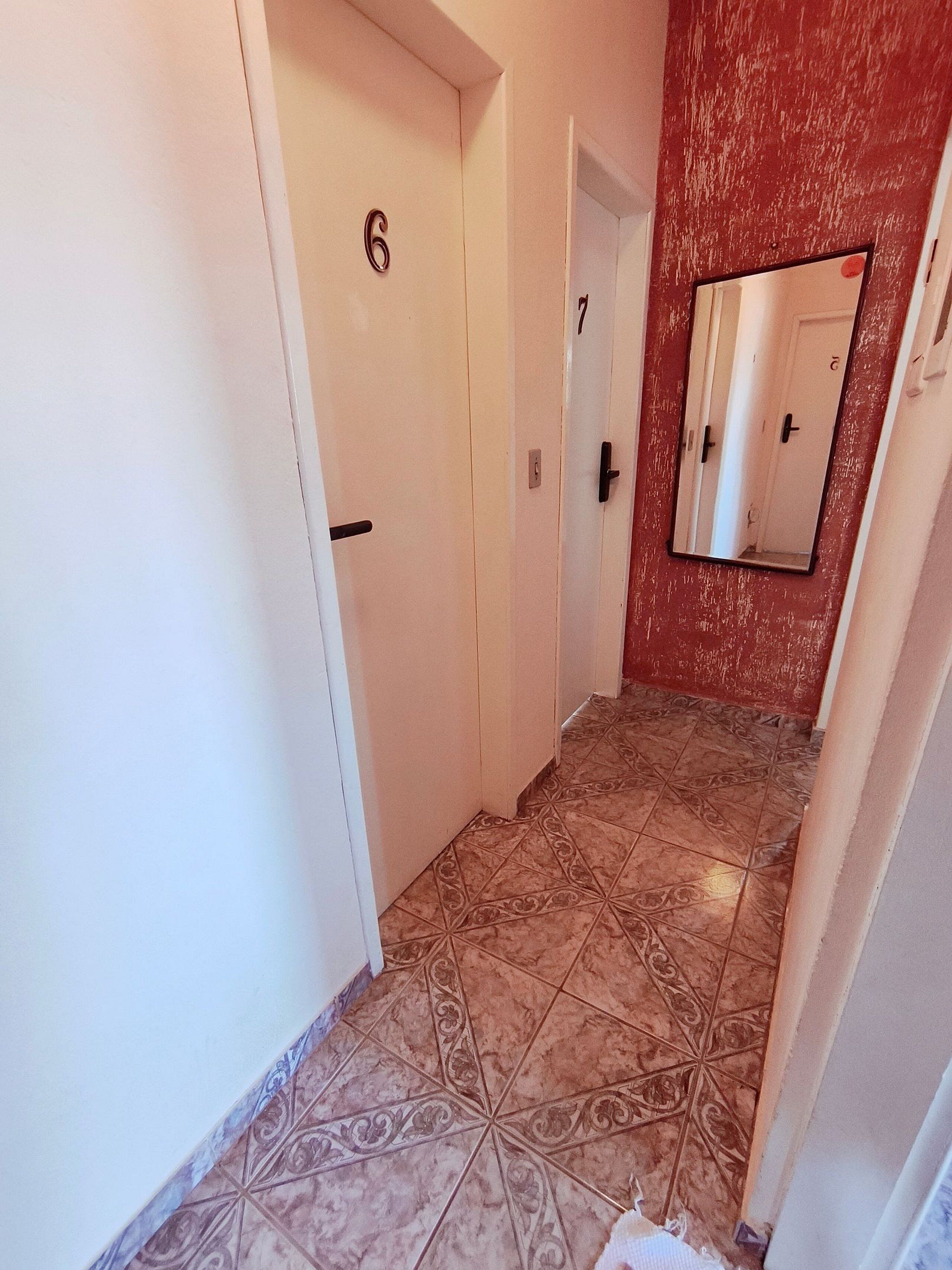 Un pasillo con puertas numeradas, suelo de baldosas y un espejo en la pared.