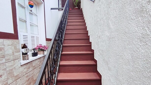 A staircase with red steps and a black railing, leading to a landing with a hanging light fixture. - CODE IN HOSPEDARIA  (Ouro Preto)