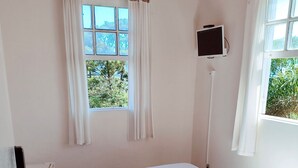 A single bed with a white mattress and a heart-patterned pillow, a television mounted on the wall, and a window with curtains. - CODE IN HOSPEDARIA  (Ouro Preto)