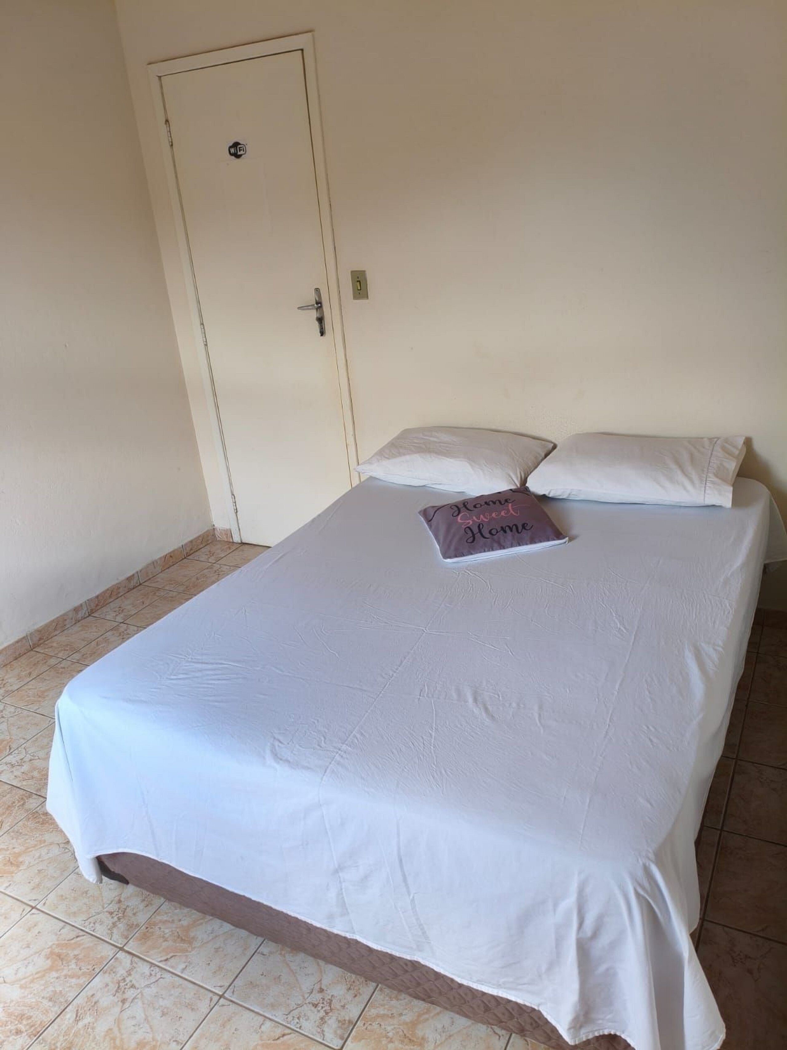A single bed with a white bedspread and two pillows, one with a printed pillowcase.