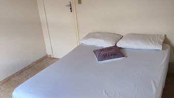 A single bed with a white bedspread and two pillows, one with a printed pillowcase.