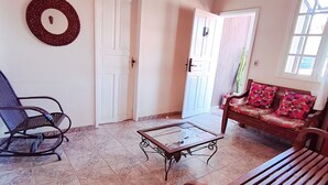 A living room with a glass-top coffee table, a wooden bench, a blue rocking chair, and a sofa with patterned cushions. - CODE IN HOSPEDARIA  (Ouro Preto)