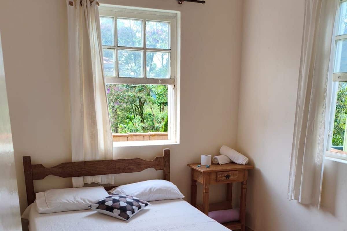 A neatly made bed with a wooden headboard, a small bedside table with a lamp, and a window with curtains.
