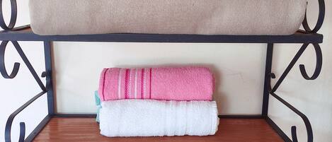 A metal shelf with three towels stacked on top and a roll of toilet paper on the bottom shelf.