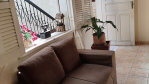 A brown sofa in a room with a tiled floor, a window with a view of a building, a door, and a potted plant. - CODE IN HOSPEDARIA  (Ouro Preto)