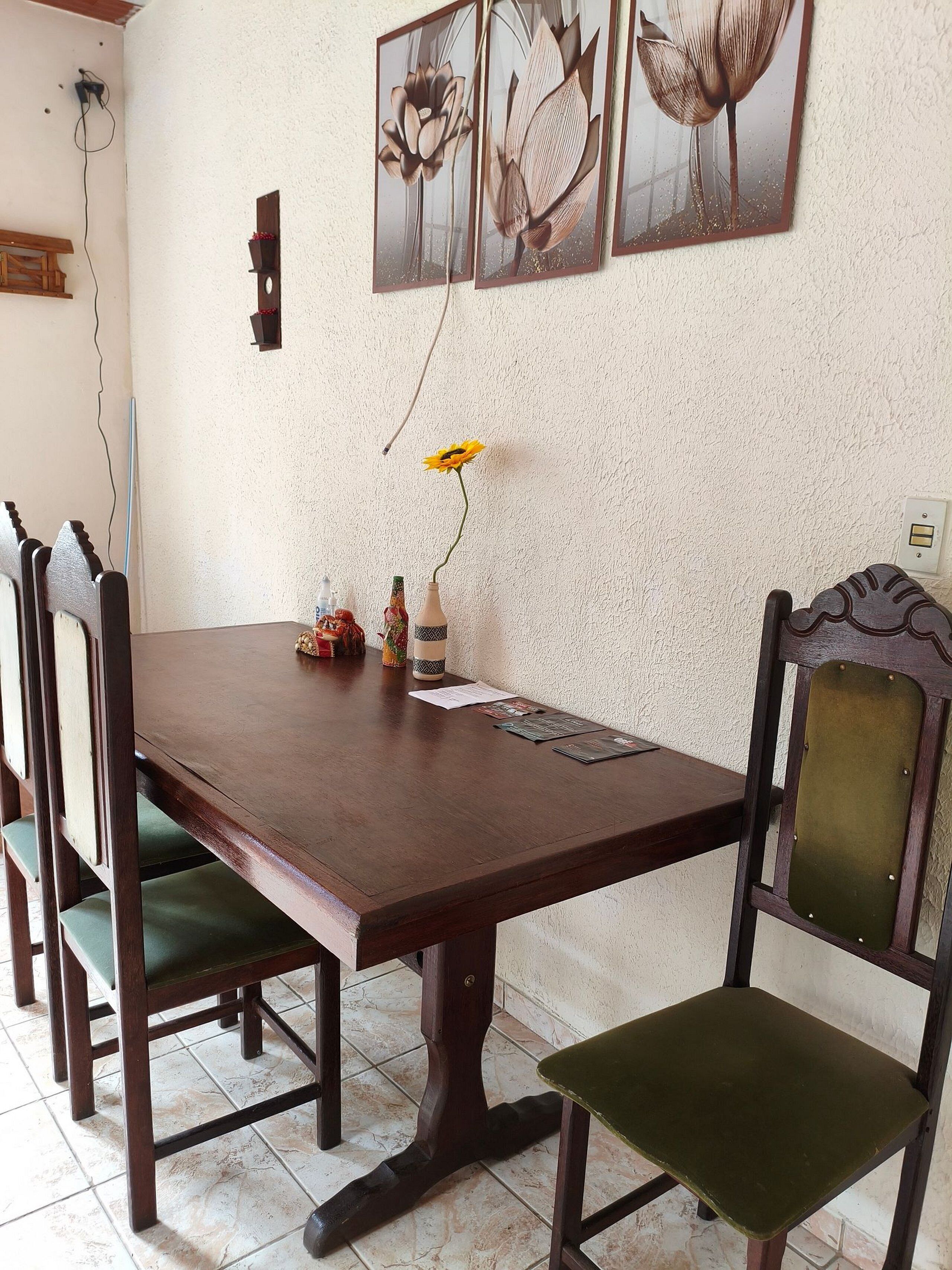 Comedor con mesa de madera, cuatro sillas y un jarrón con una sola flor amarilla.