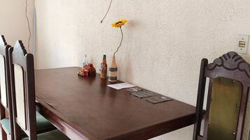 Comedor con mesa de madera, cuatro sillas y un jarrón con una sola flor amarilla.