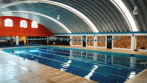 An indoor swimming pool with a high, curved metal roof and brick walls.