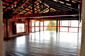 A spacious room with wooden floors, large windows, and a high ceiling with exposed beams.