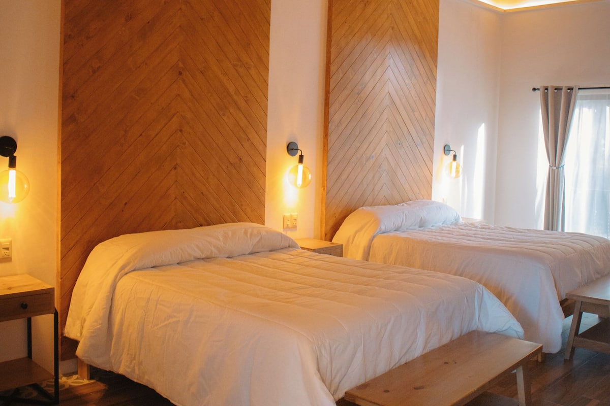 A room with two beds, wooden flooring, a bench, and a herringbone-patterned wall.