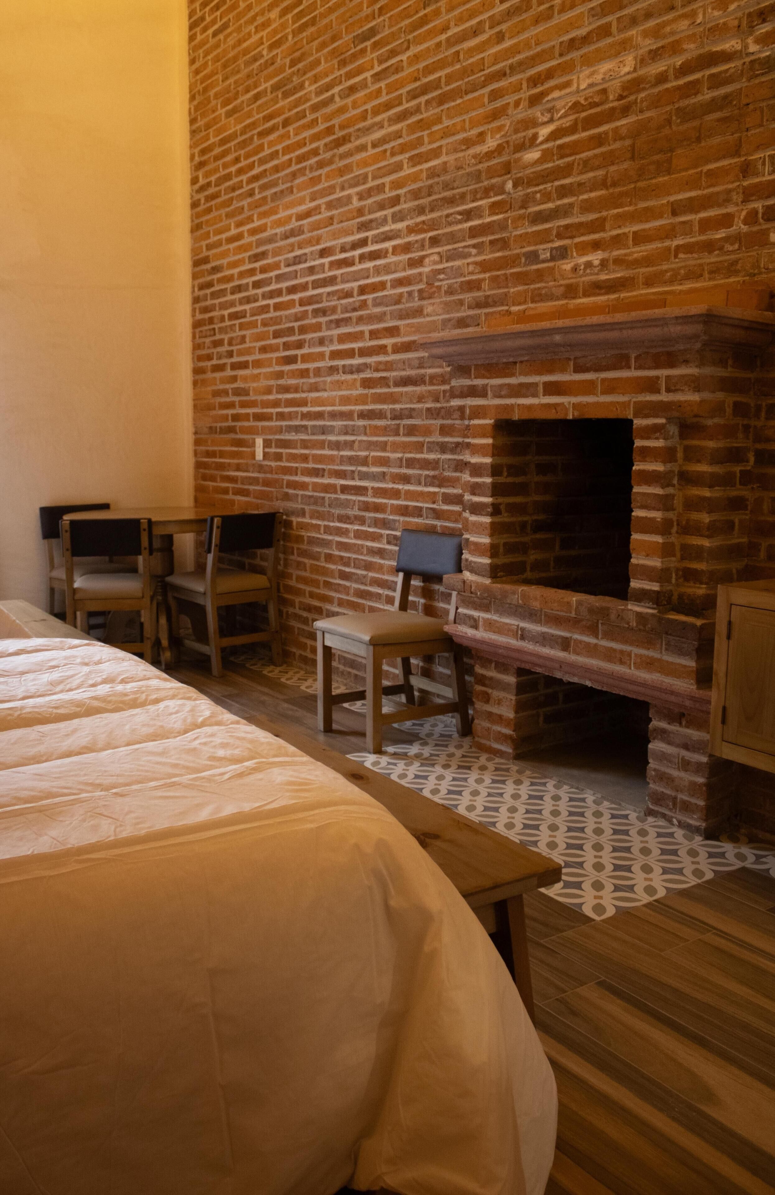 Une pièce avec une cheminée en briques, un lit, une table en bois et deux chaises.
