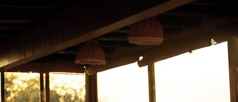 Un comedor con sillas y mesas de madera, ventanas amplias y vistas a árboles desde el exterior.