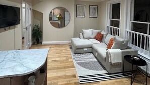 Un saló modern amb un sofà modular, una illa de cuina de marbre i un mirall gran.