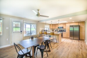 A modern kitchen with wooden cabinets, a stainless steel refrigerator, and a dining area with a wooden table and chairs.