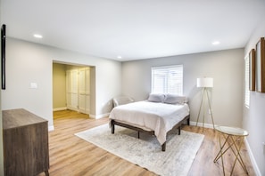 A bedroom with a bed, bedside table, lamp, and a view of a hallway.