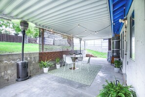 A covered patio area with a table and chairs, a heater, and potted plants.