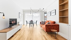 A modern living room with a sofa, a TV, a dining table with chairs, and a wooden floor.
