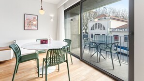 A modern dining area with a round table and green chairs, a framed picture on the wall, and a large sliding glass door leading to an outdoor balcony.