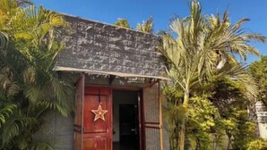 A small building with a red door and a star emblem, surrounded by palm trees and a well-maintained lawn. - Rancho de 3 dormitorios en la Costa del Sol, La Paz. con aire acondicionado (El zapote)