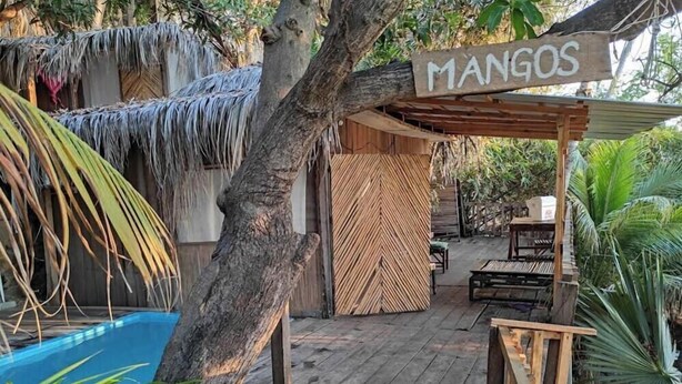 Una terraza de madera con un letrero que dice "MANGOS", una piscina y un área de estar cubierta.