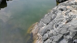 Orilla rocosa con agua cristalina que refleja el cielo.