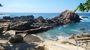 Una zona costera rocosa con vista despejada al océano, destacando una formación rocosa prominente y un sendero de piedra que conduce al agua.