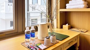 A hotel room with a wooden desk, a vase with branches, a stack of towels, and a window with a view of buildings. - Peace Home Boutique Hotel (Phu Thuy)