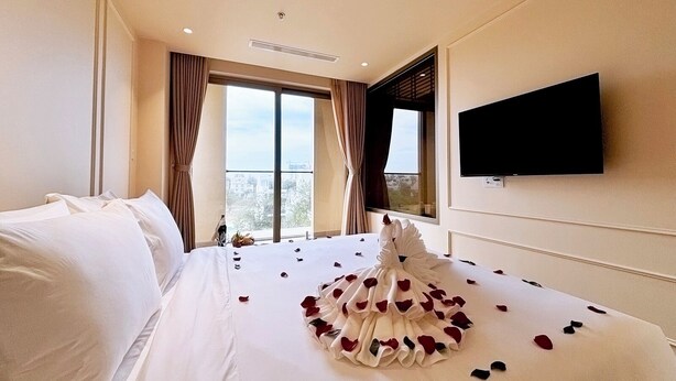 A hotel room with a large bed, a flat-screen TV mounted on the wall, and a window with curtains. - Peace Home Boutique Hotel (Phu Thuy)