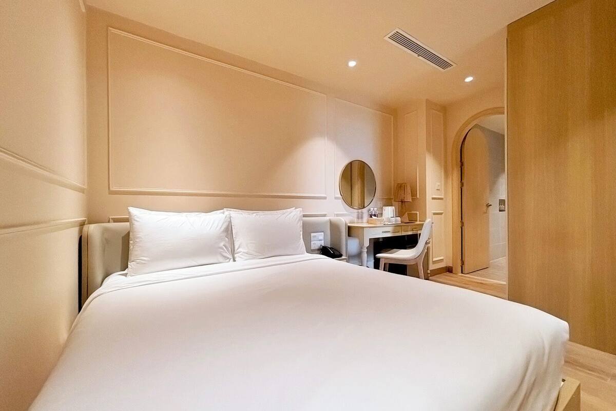 Hotellihuone, jossa on suuri sänky, työpöytä tuolilla, peili ja ovi, joka johtaa toiseen huoneeseen.