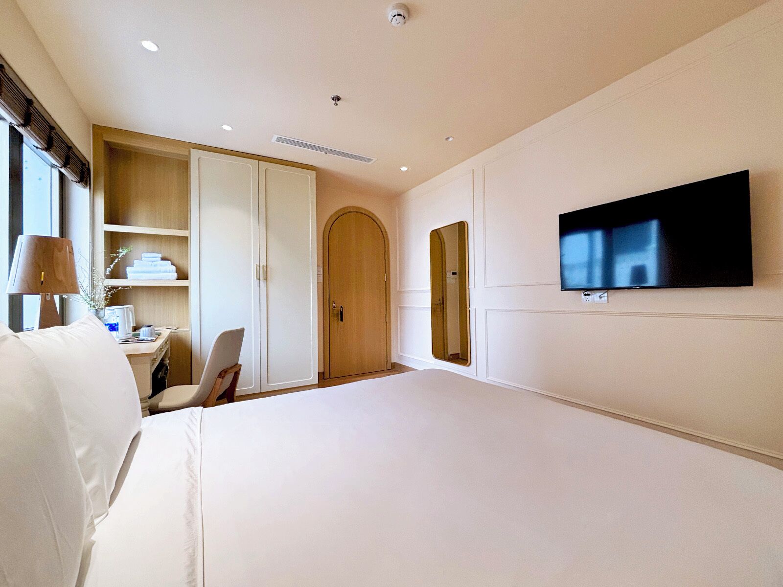 A hotel room with a bed, a desk, a wardrobe, a television, and a mirror.