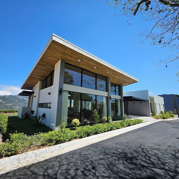 A modern two-story building with large glass windows, a flat roof, and a well-maintained garden.