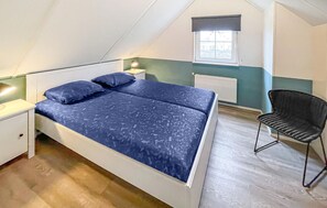 Un dormitorio con cama, mesita de noche, silla, ventana, radiador y techo inclinado.
