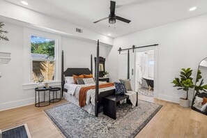 Ein Schlafzimmer mit Himmelbett, Deckenventilator, großem Fenster und Blick auf Grünlandschaft.